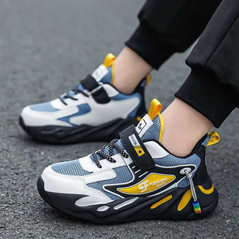 Boys sports running shoes in dark blue with a mesh upper and Velcro strap, shown on a hard ground surface.