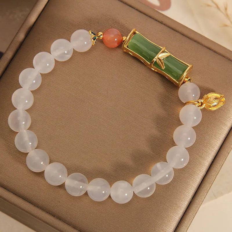 A women's bracelet with a textured jade bamboo bead and a white agate charm on a beaded string.