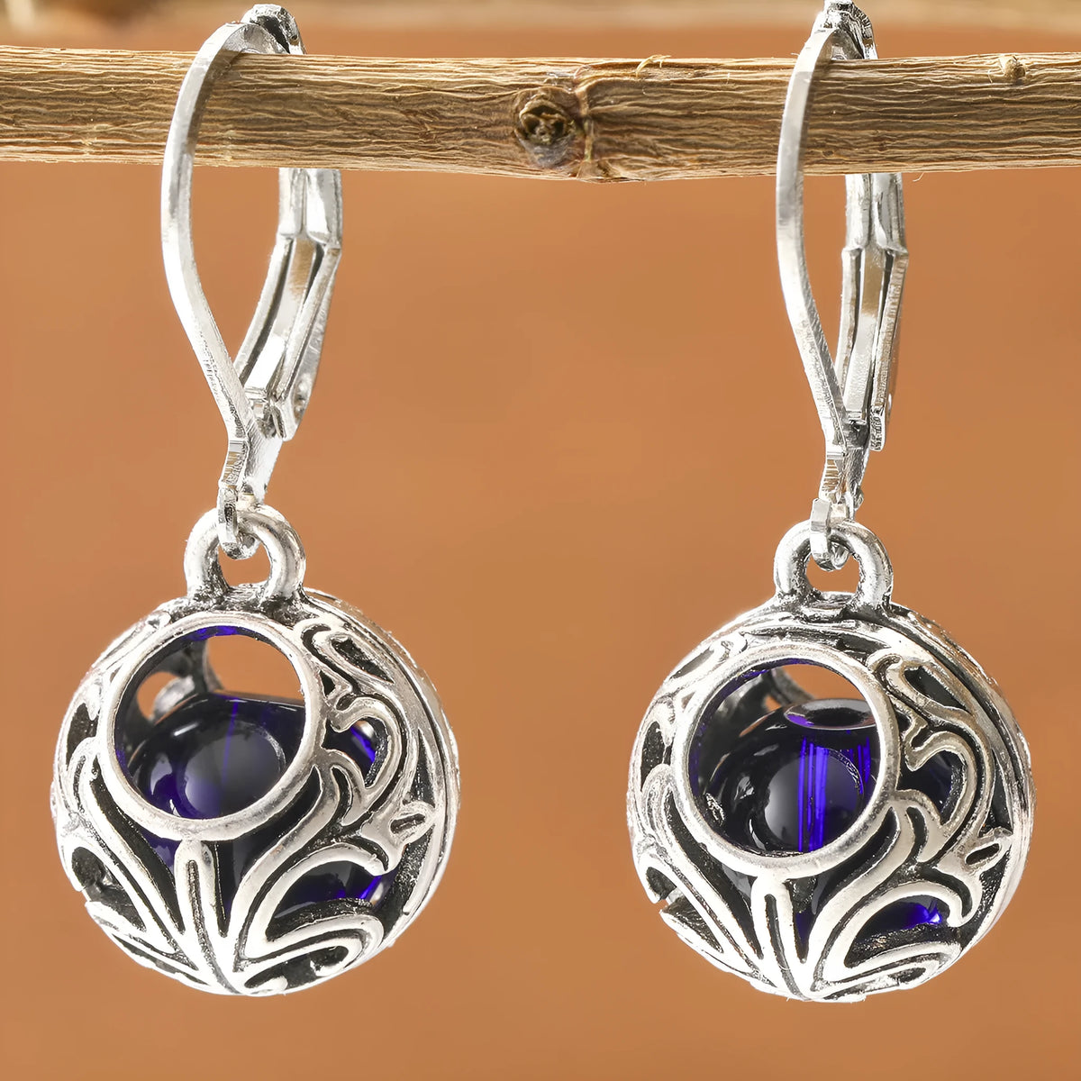Silver geometric hollow pendant earrings with vintage engraving and a central blue gemstone on a zinc alloy setting.