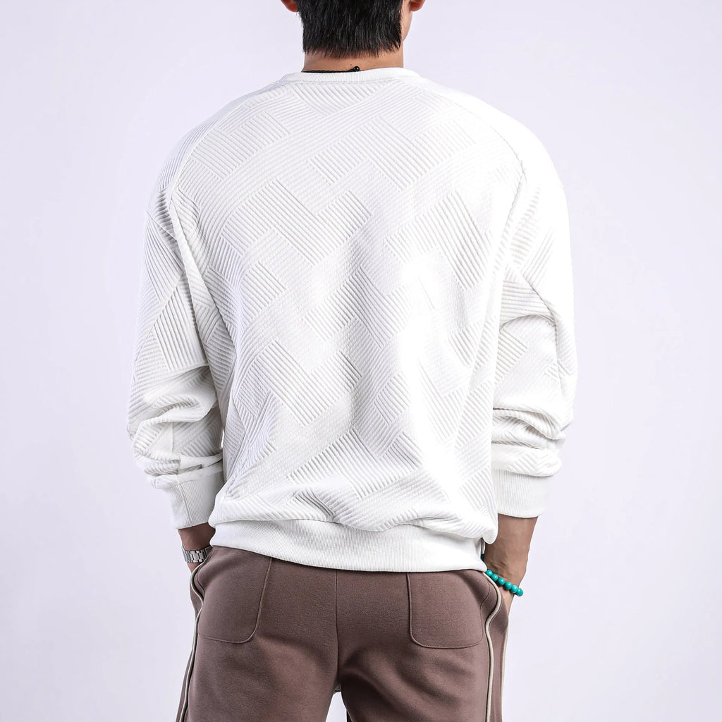 Man wearing a loose grey twill jacquard pullover sweater with a round neck and long sleeves.