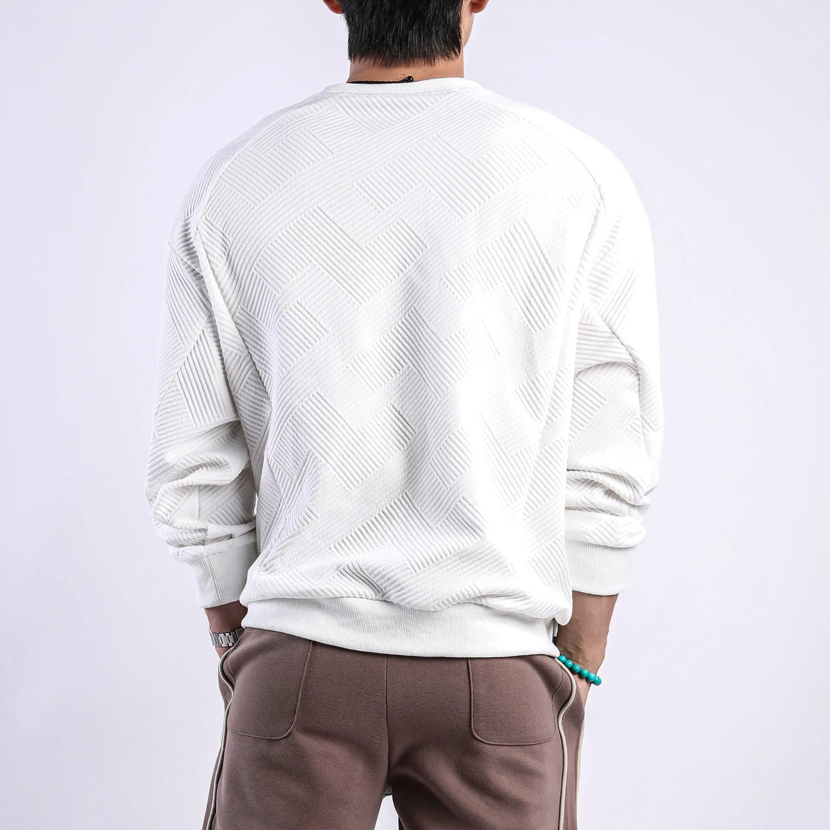 Man wearing a loose grey twill jacquard pullover sweater with a round neck and long sleeves.