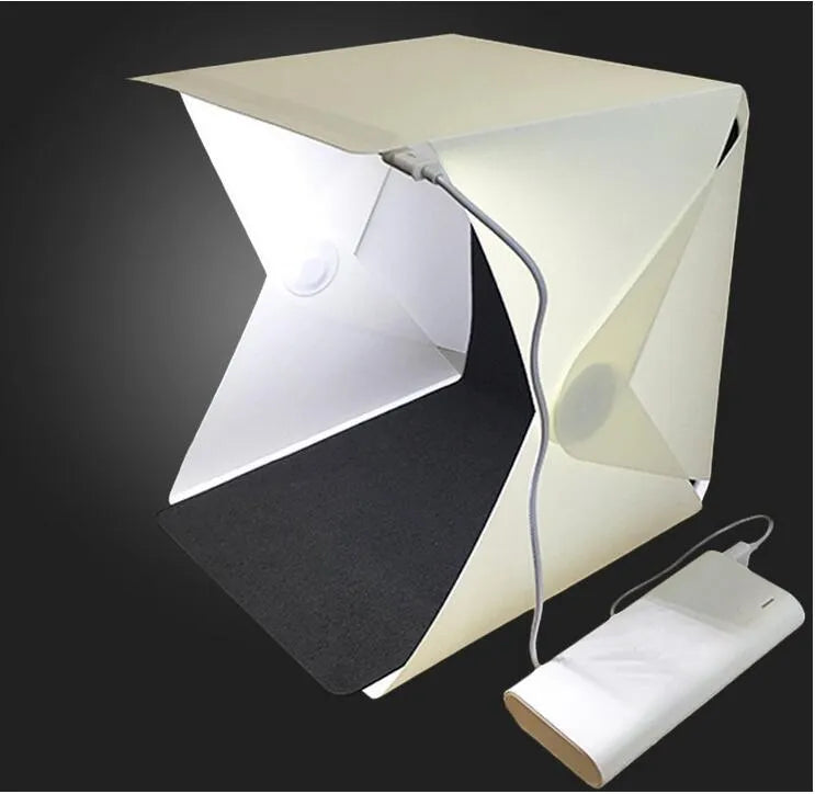 Mini LED folding photo box open with black and white background pads, USB cable, and built-in light for small item photography