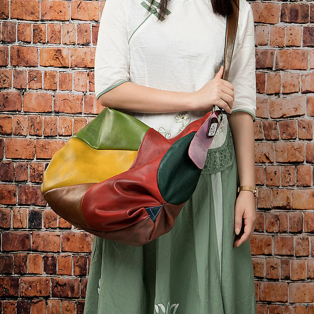 Brown cowhide leather crossbody travel bag with stitching, holding a laptop and magazine.