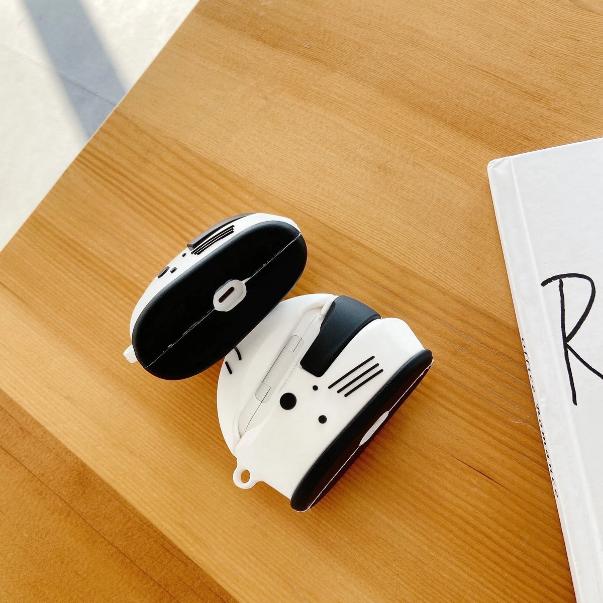 Black silicone AirPods case with motorcycle helmet shape, cartoon geometric design, and carabiner clip