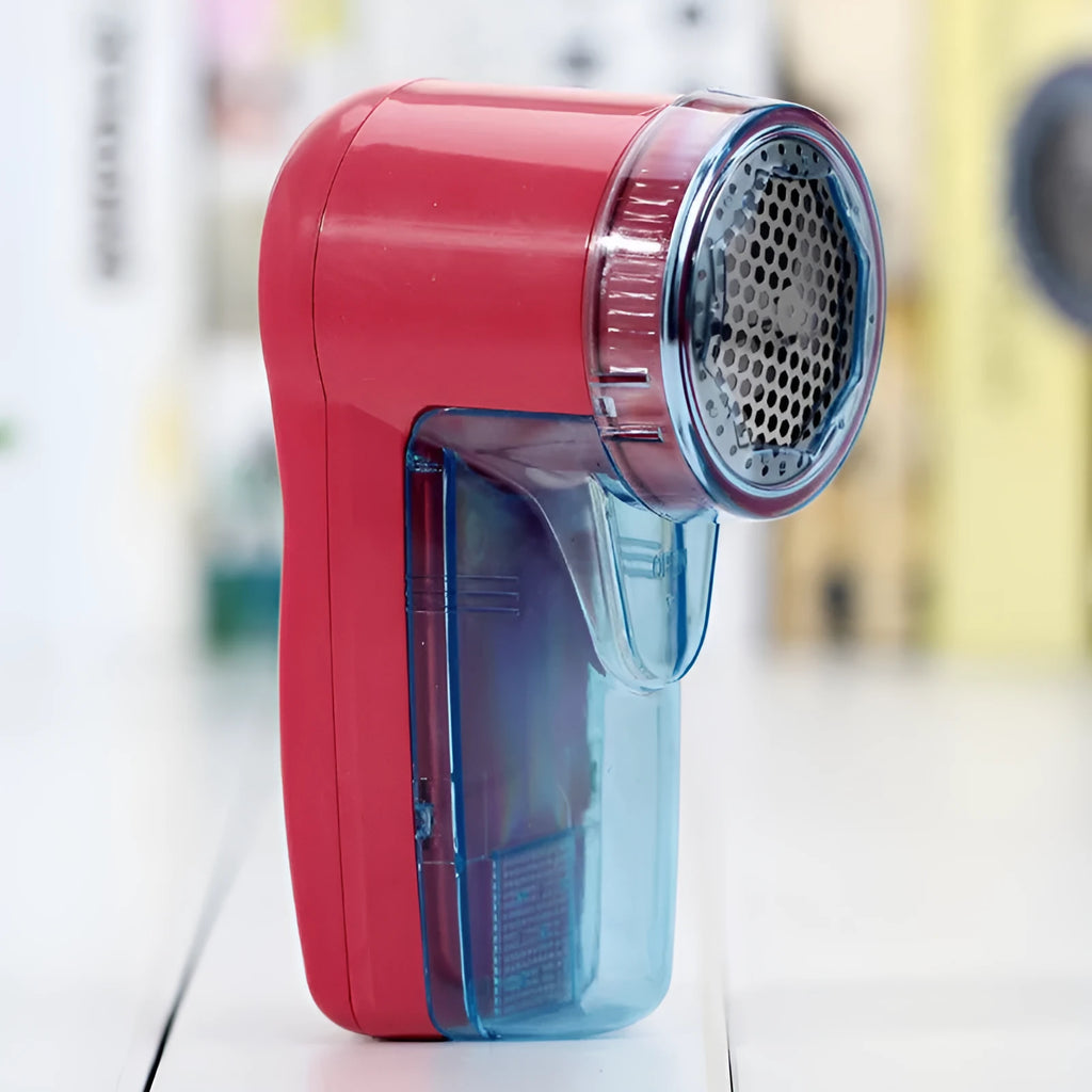 Portable electric clothing lint remover device on a table next to a sweater.