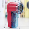 Portable electric clothing lint remover device on a table next to a sweater.