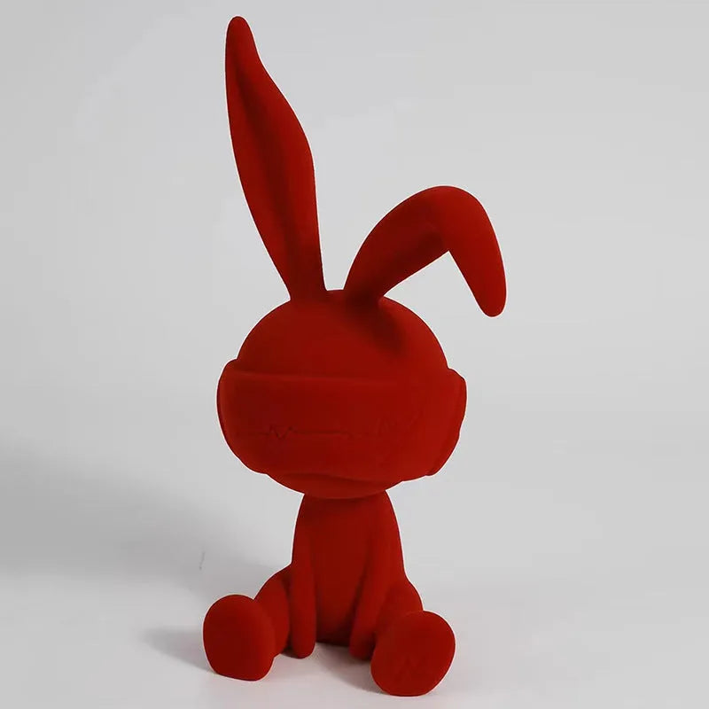 A resin table ornament of a rabbit wearing a suede blindfold, shown in blue, green, and red colour options.