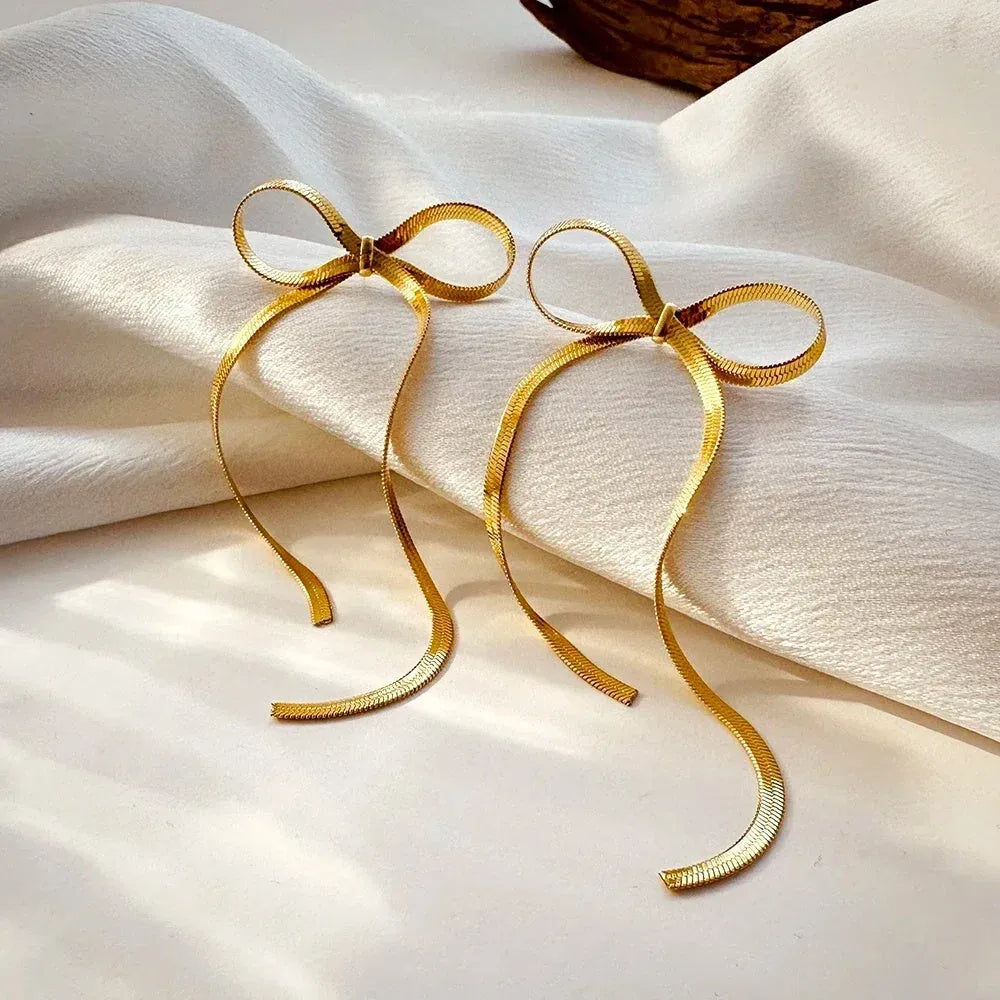 Gold plated bow ribbon dangle earrings with tassel tails on white background