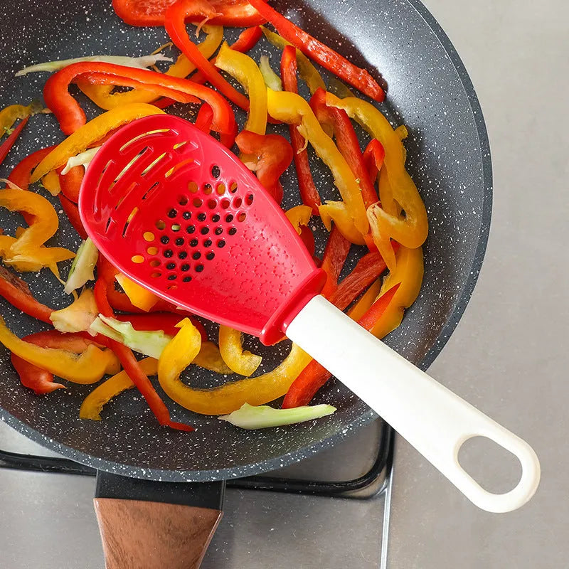 Red and black multifunctional plastic cooking spoon with serrated edges and slotted head on a grey background