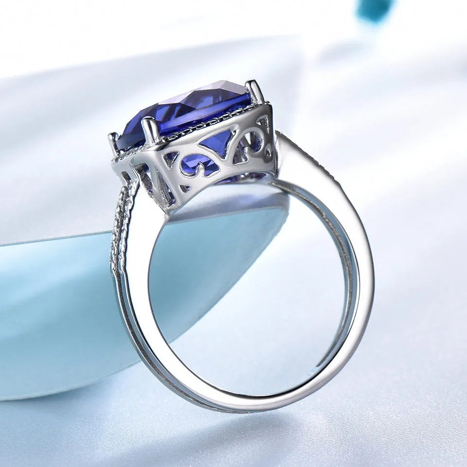 Blue tanzanite gemstone set in a silver women's ring on a finger.