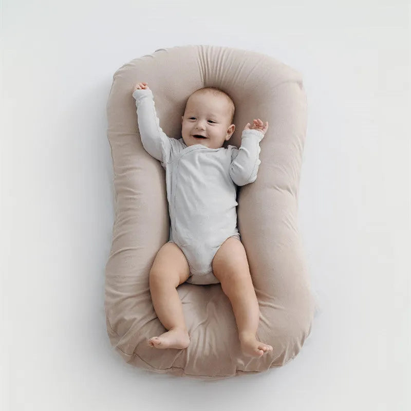 Beige portable cotton baby nest crib for newborns on a neutral background
