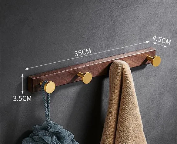 A row of black walnut bathroom clothes hooks with brushed brass metal details on a perforated mounting strip.