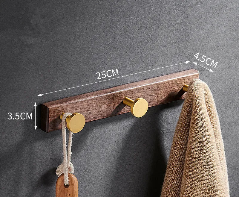A row of black walnut bathroom clothes hooks with brushed brass metal details on a perforated mounting strip.