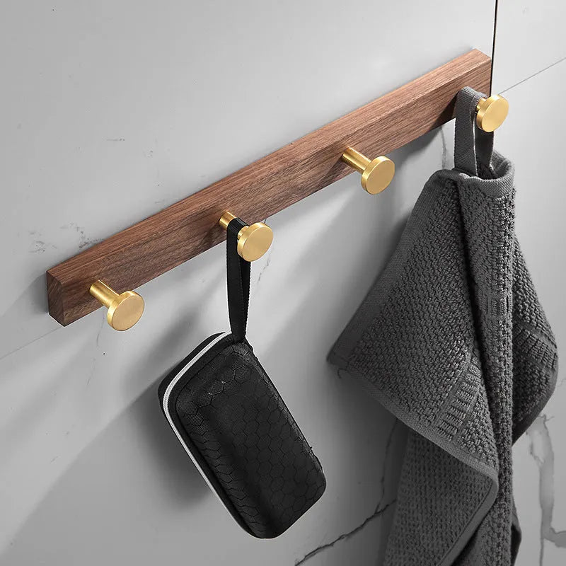 A row of black walnut bathroom clothes hooks with brushed brass metal details on a perforated mounting strip.
