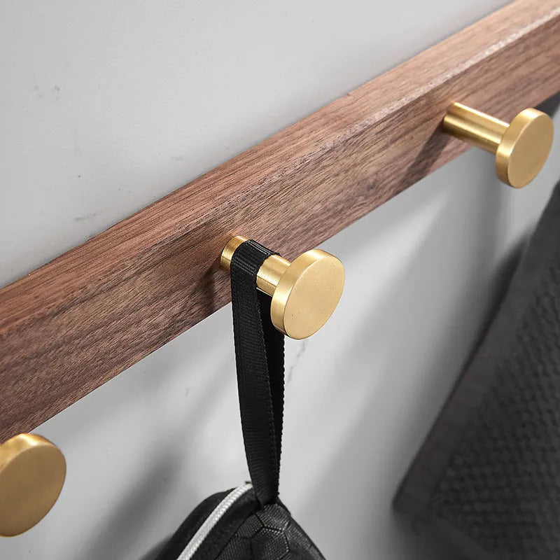 A row of black walnut bathroom clothes hooks with brushed brass metal details on a perforated mounting strip.