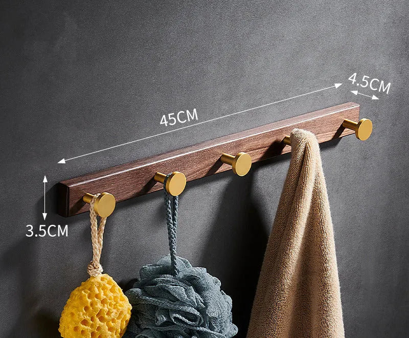 A row of black walnut bathroom clothes hooks with brushed brass metal details on a perforated mounting strip.