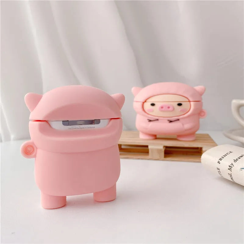 Pink silicone AirPods case with cartoon pig in sweater design, shown with flip lid open and a matching metal hook.