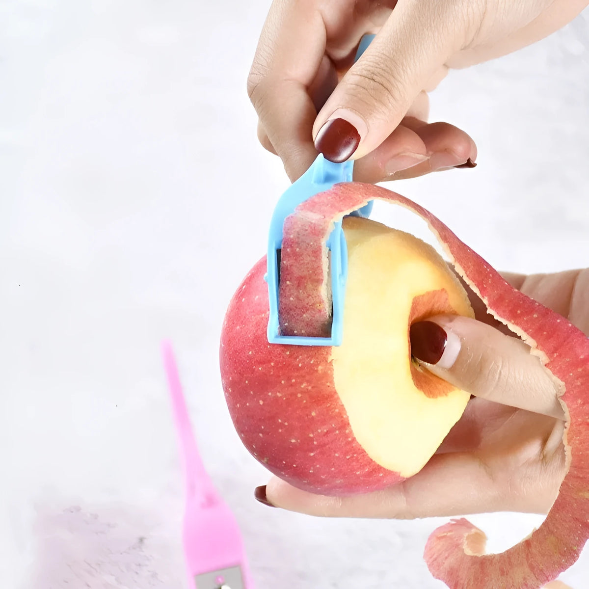 Finger ring peeler with plastic body and stainless steel blade in pink, blue, or orange for scraping fruit and vegetable skin