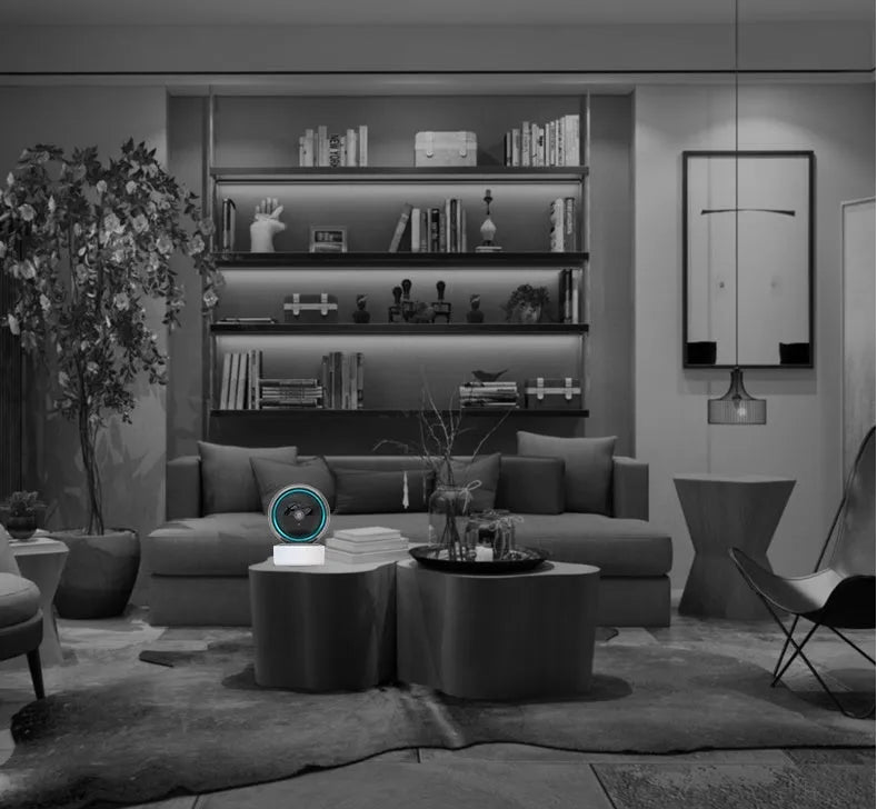White 360-degree rotating indoor Wi-Fi security camera on a table with a UK plug power cord.