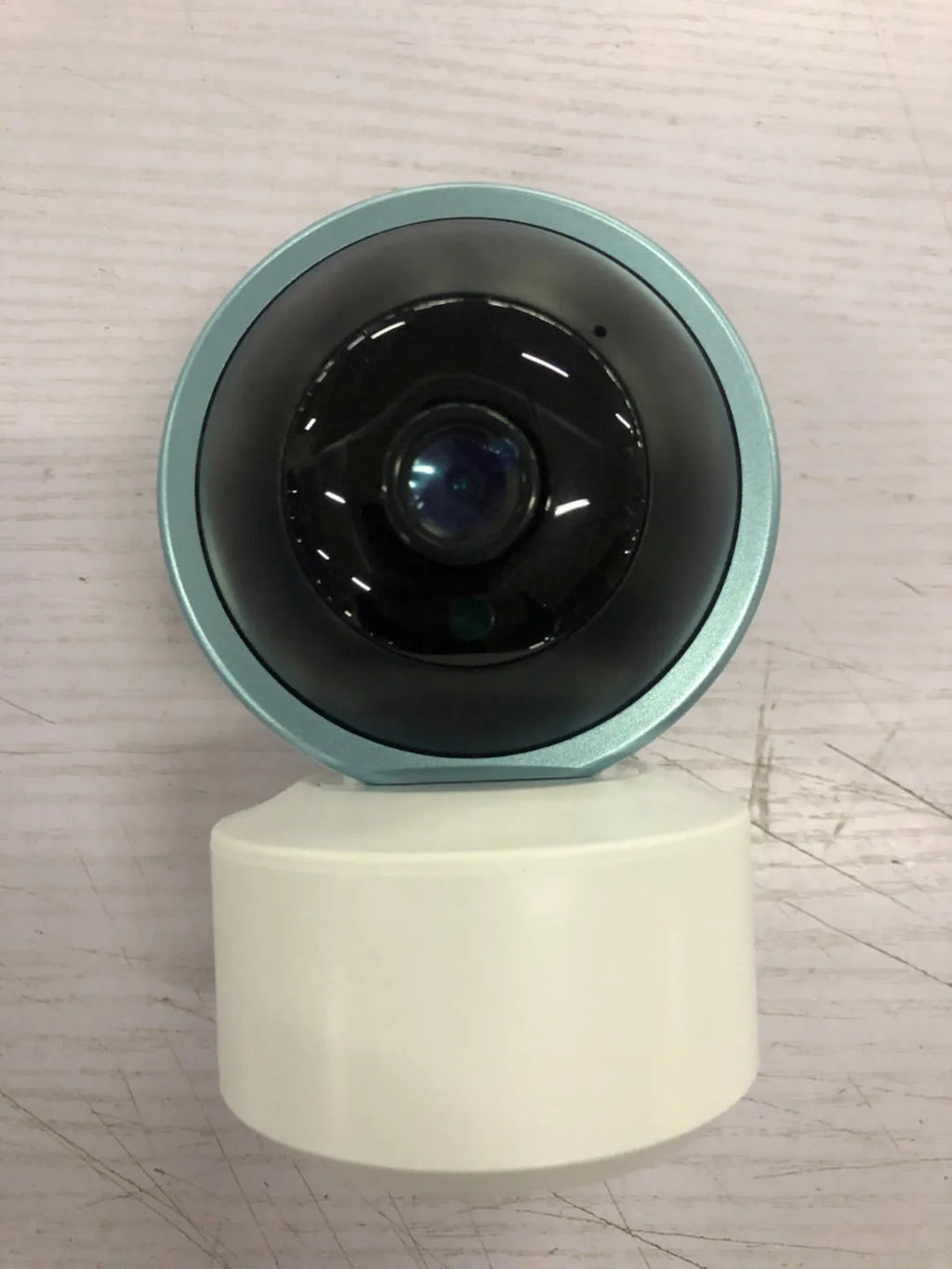 White 360-degree rotating indoor Wi-Fi security camera on a table with a UK plug power cord.