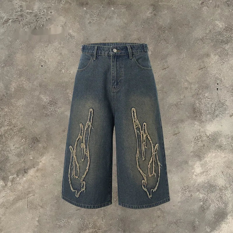 Men's black cropped denim shorts with a flame embroidery patch on the leg, showing straight cut.