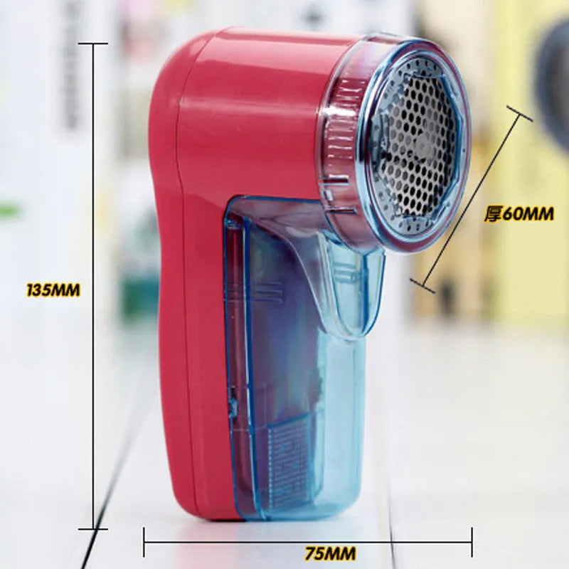Portable electric clothing lint remover device on a table next to a sweater.