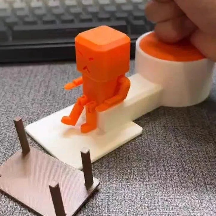 Orange plastic decompression toy with a table-turning mechanism on a desk.