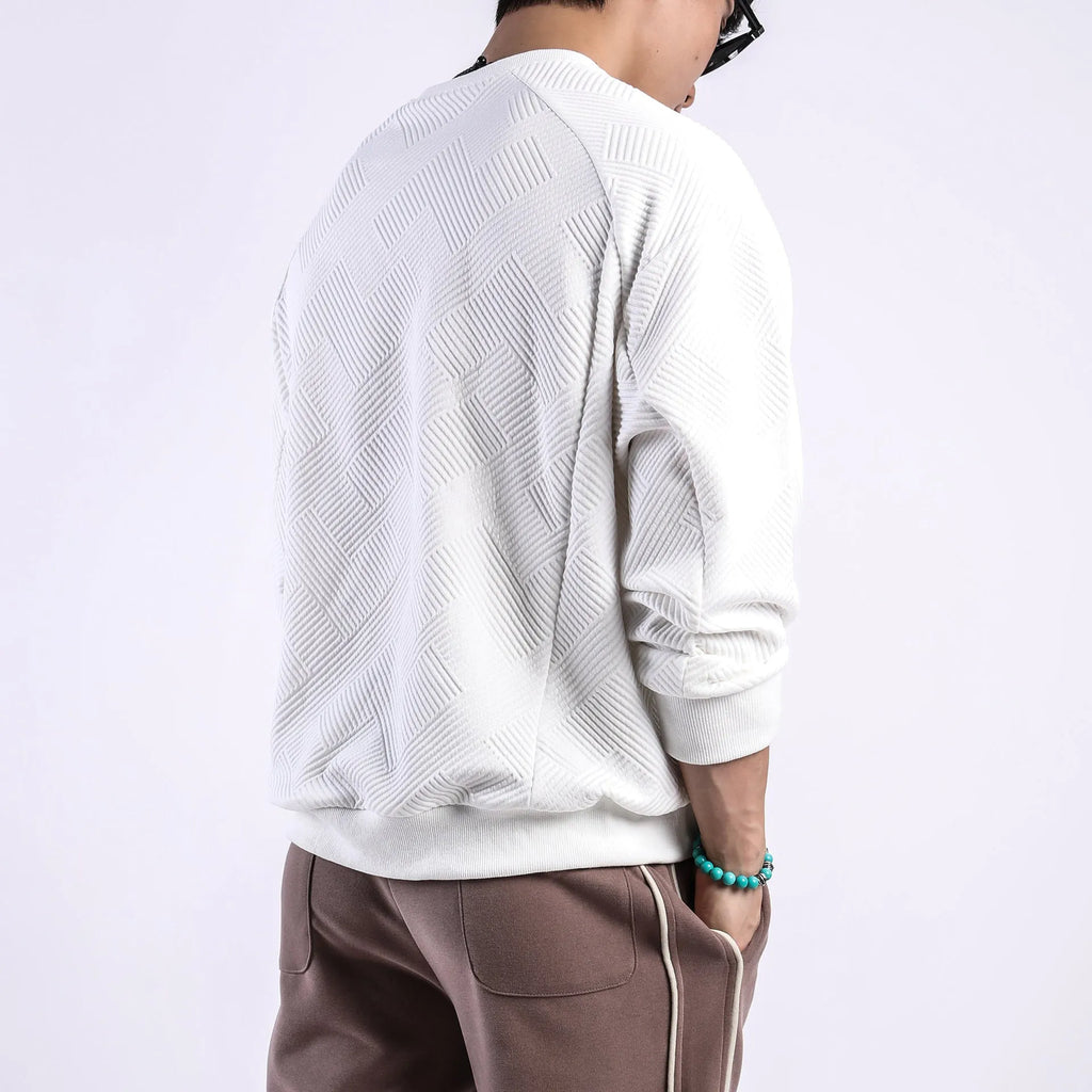 Man wearing a loose grey twill jacquard pullover sweater with a round neck and long sleeves.