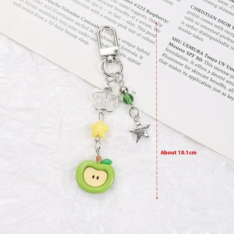 Red apple and strawberry plastic phone charm keychain with white rope on a mobile phone.