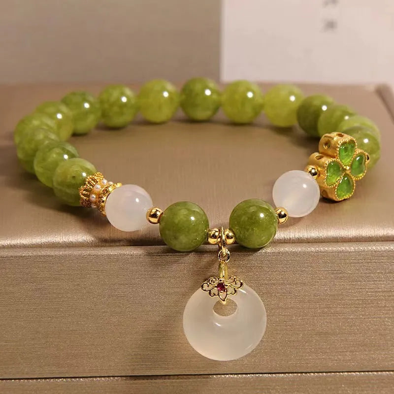 Women's green tourmaline bracelet with a four-leaf clover charm and safety buckle on a wrist.