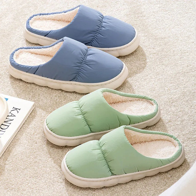 A pair of blue down cotton plush slippers with a thick rubber sole and artificial leather upper, shown on a wooden floor.