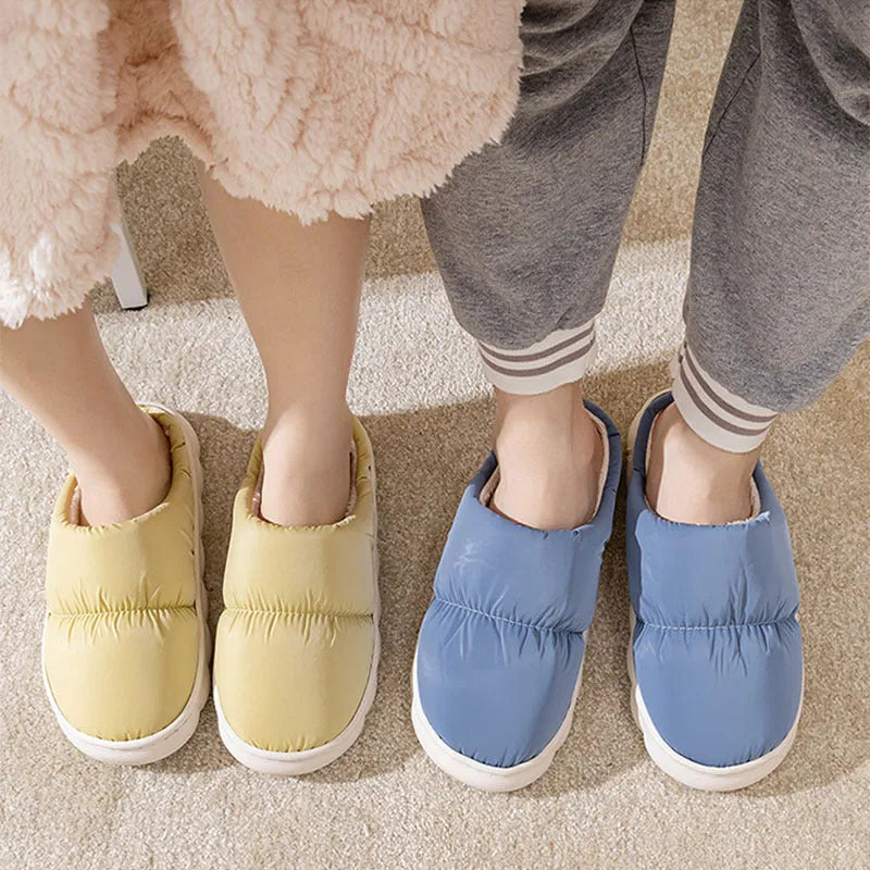 A pair of blue down cotton plush slippers with a thick rubber sole and artificial leather upper, shown on a wooden floor.