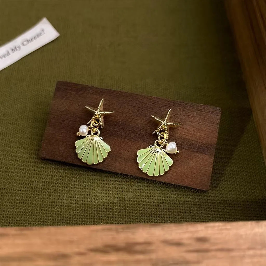 14K gold starfish shell earrings in light green on a white background
