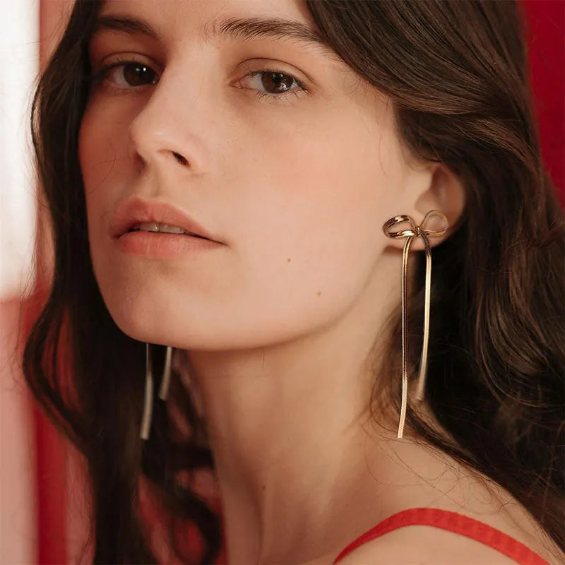 Gold plated bow ribbon dangle earrings with tassel tails on white background