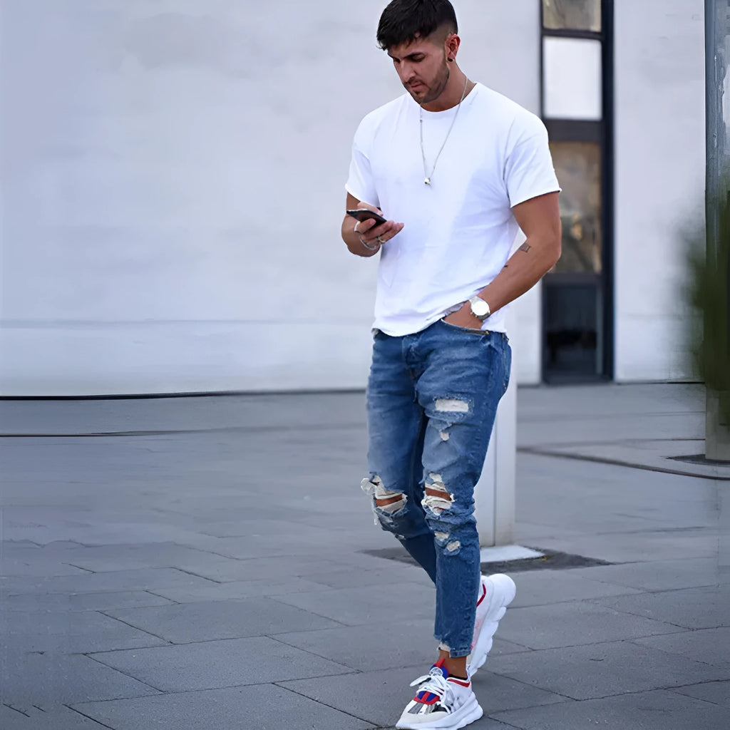 Deep blue men's jeans with distressed hole details and five pockets laid flat.