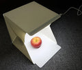Mini LED folding photo box open with black and white background pads, USB cable, and built-in light for small item photography