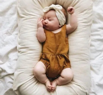 Beige portable cotton baby nest crib for newborns on a neutral background