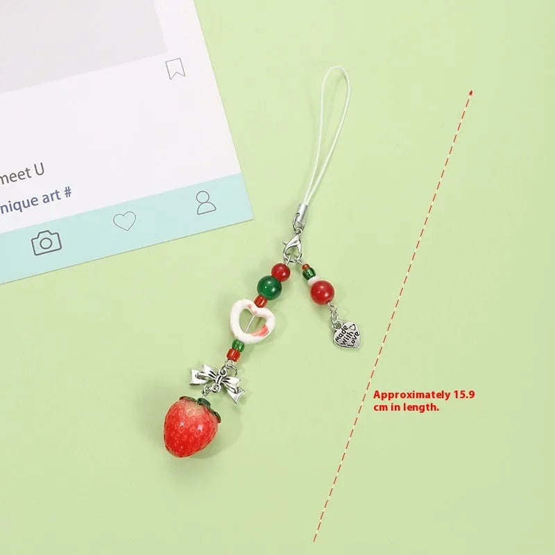 Red apple and strawberry plastic phone charm keychain with white rope on a mobile phone.