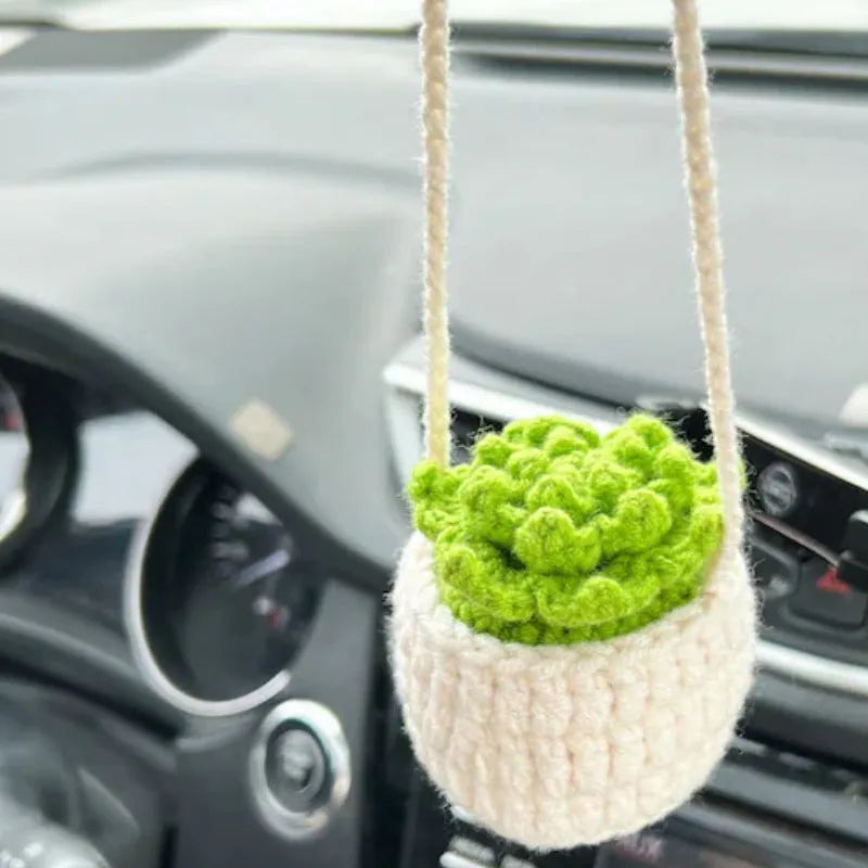 Green and white knitted wool car plant ornament with basin base and hanging rope.