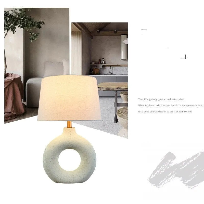 Small white Japanese style pottery pot table lamp with a button switch on a desk.