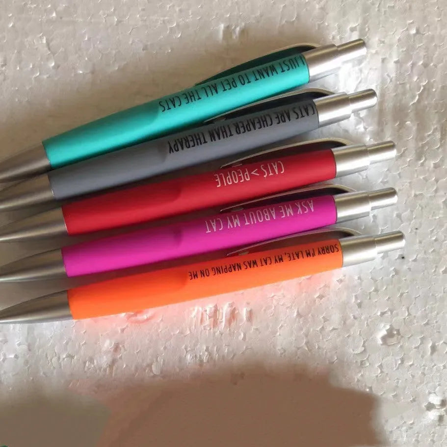 Set of five coloured push action automatic pens in a cat-themed or dog-themed design, next to a beaded storage bag.