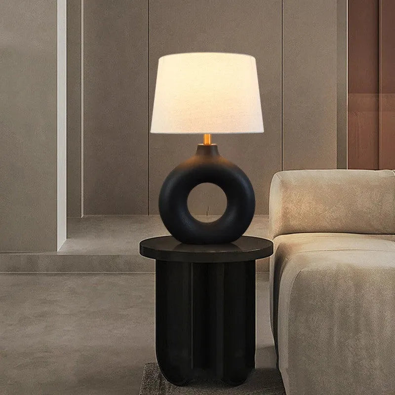 Small white Japanese style pottery pot table lamp with a button switch on a desk.