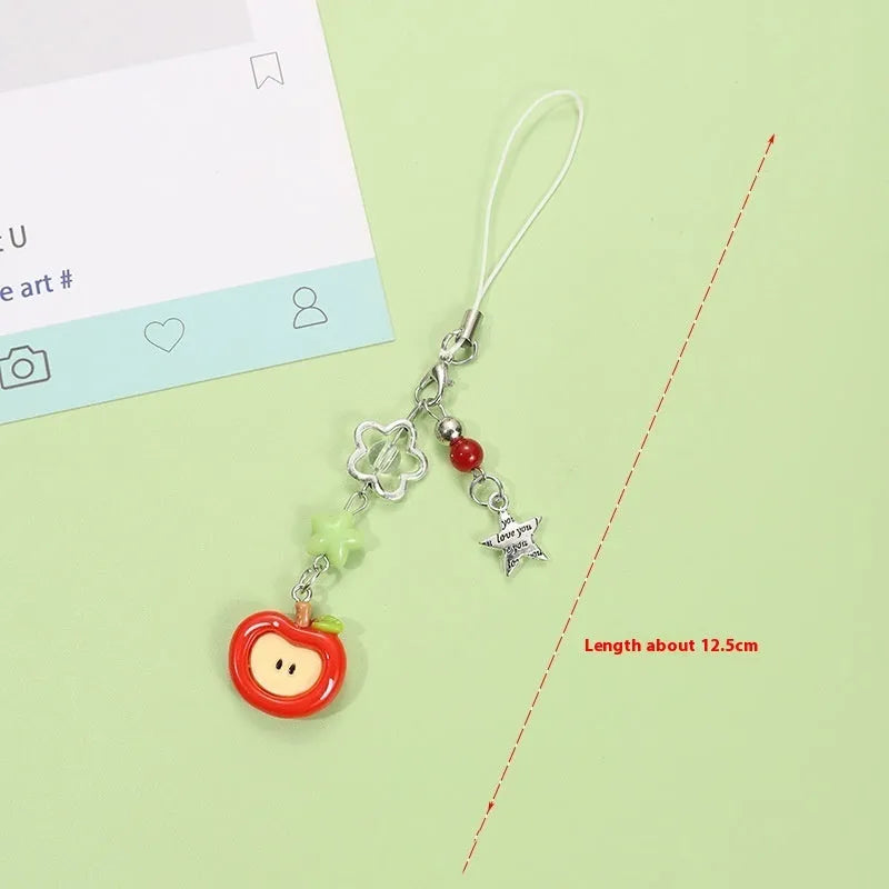 Red apple and strawberry plastic phone charm keychain with white rope on a mobile phone.