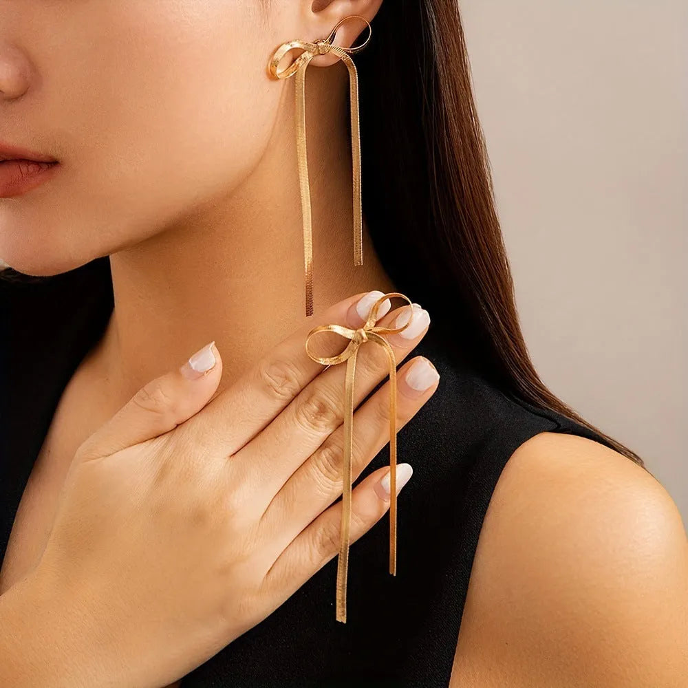 Gold plated bow ribbon dangle earrings with tassel tails on white background