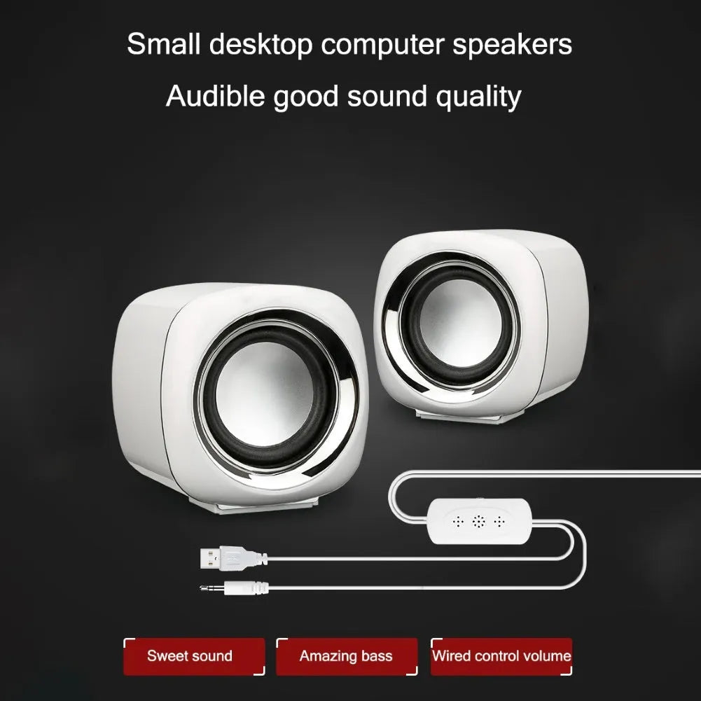 A pair of compact black or white wired desktop computer speakers with a 3.5mm plug, shown next to a laptop.