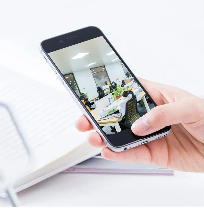 White 360-degree rotating indoor Wi-Fi security camera on a table with a UK plug power cord.
