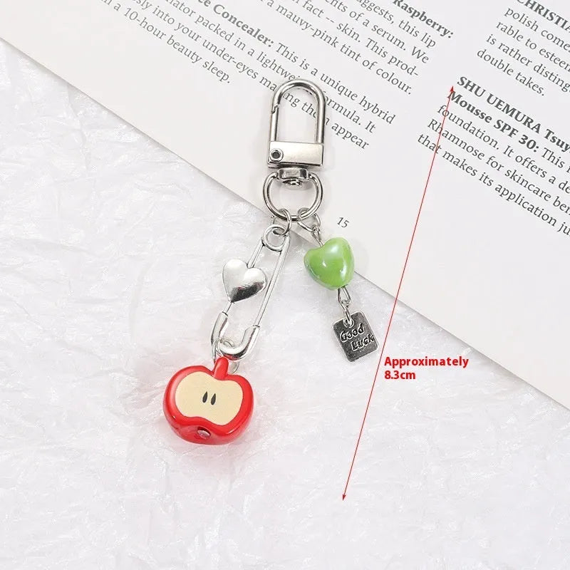 Red apple and strawberry plastic phone charm keychain with white rope on a mobile phone.