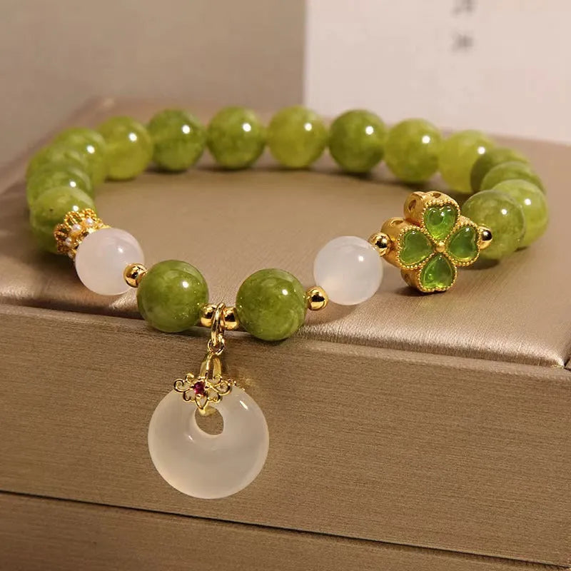 Women's green tourmaline bracelet with a four-leaf clover charm and safety buckle on a wrist.