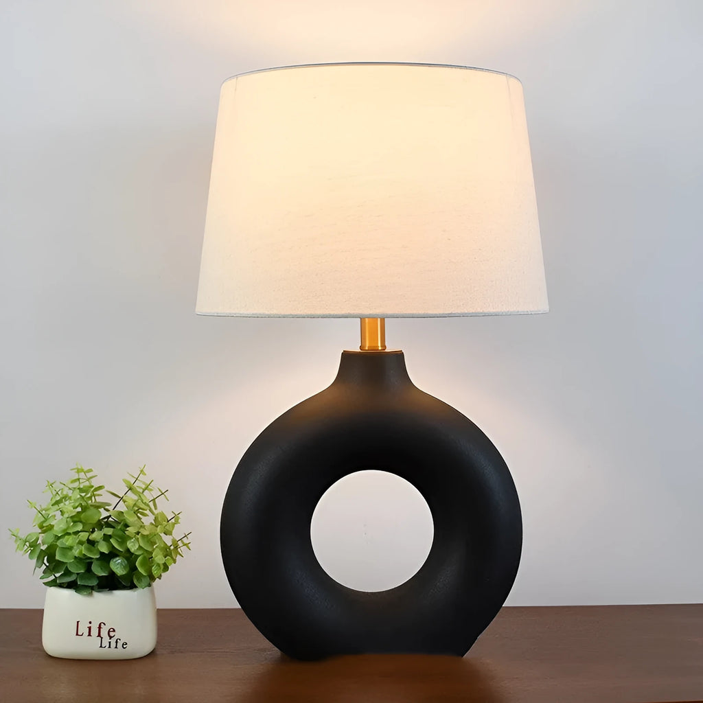 Small white Japanese style pottery pot table lamp with a button switch on a desk.