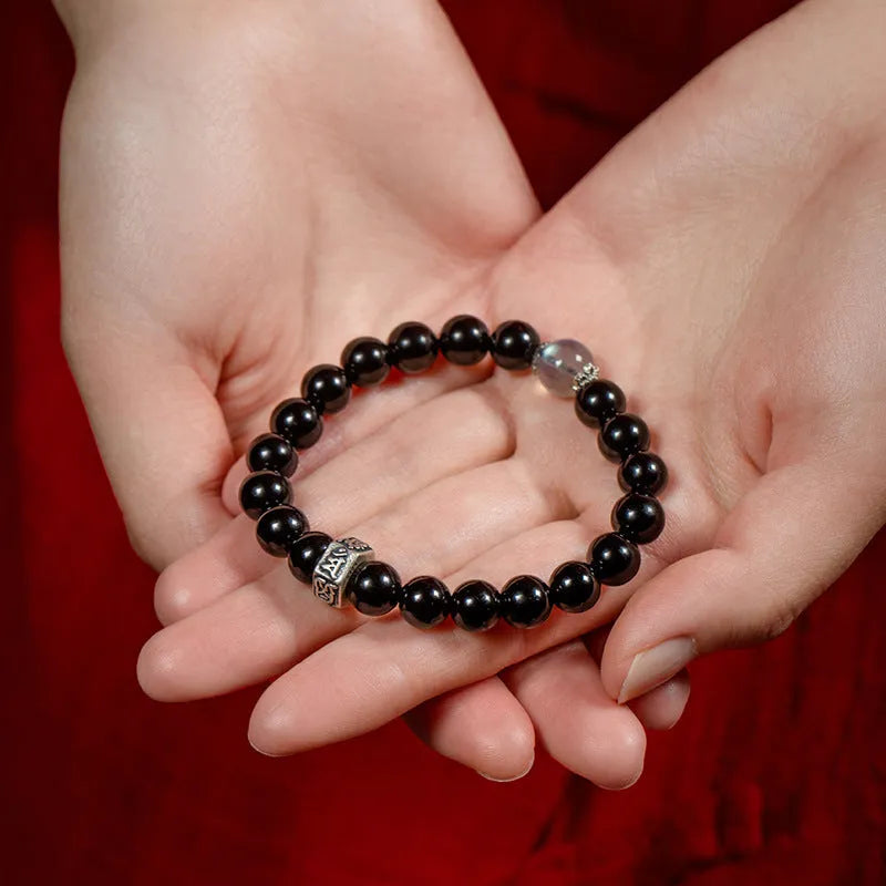 Old Pit Obsidian 8mm bead bracelet with zodiac animal charms on a wrist, showing ethnic style and unset inlaid design.